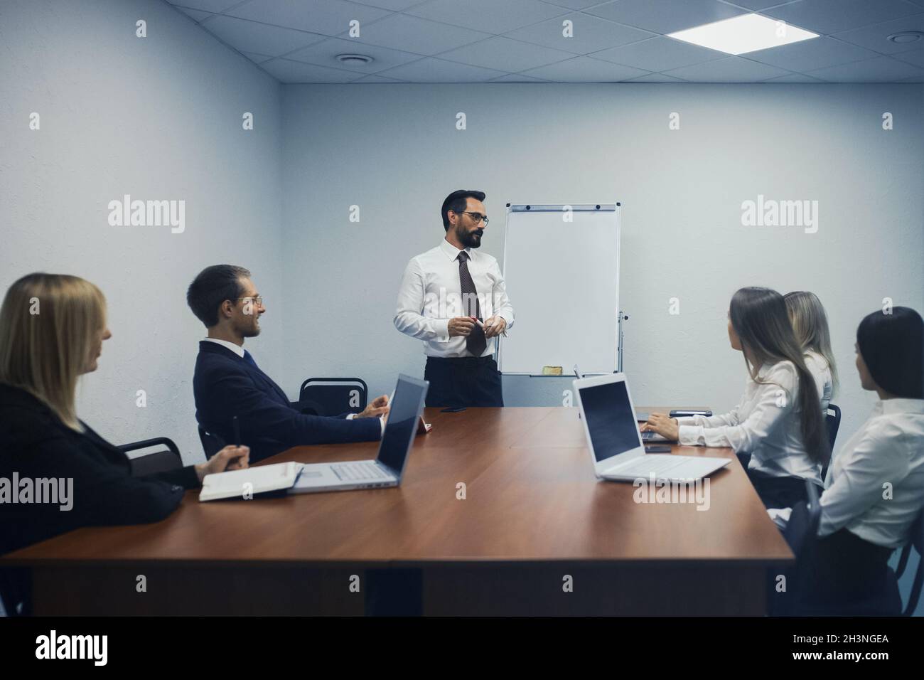 Réunion de la haute direction dans un bureau moderne.Le conférencier se tient près du tableau blanc pour discuter avec des collègues qui sont assis à deux Banque D'Images