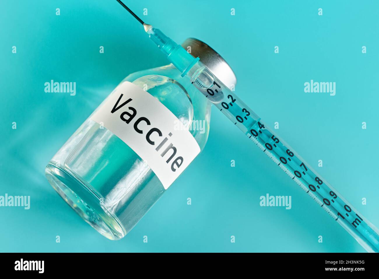 Flacon en verre avec étiquette de vaccin et aiguille de seringue hypodermique à proximité, vue du dessus sur fond vert cyan Banque D'Images