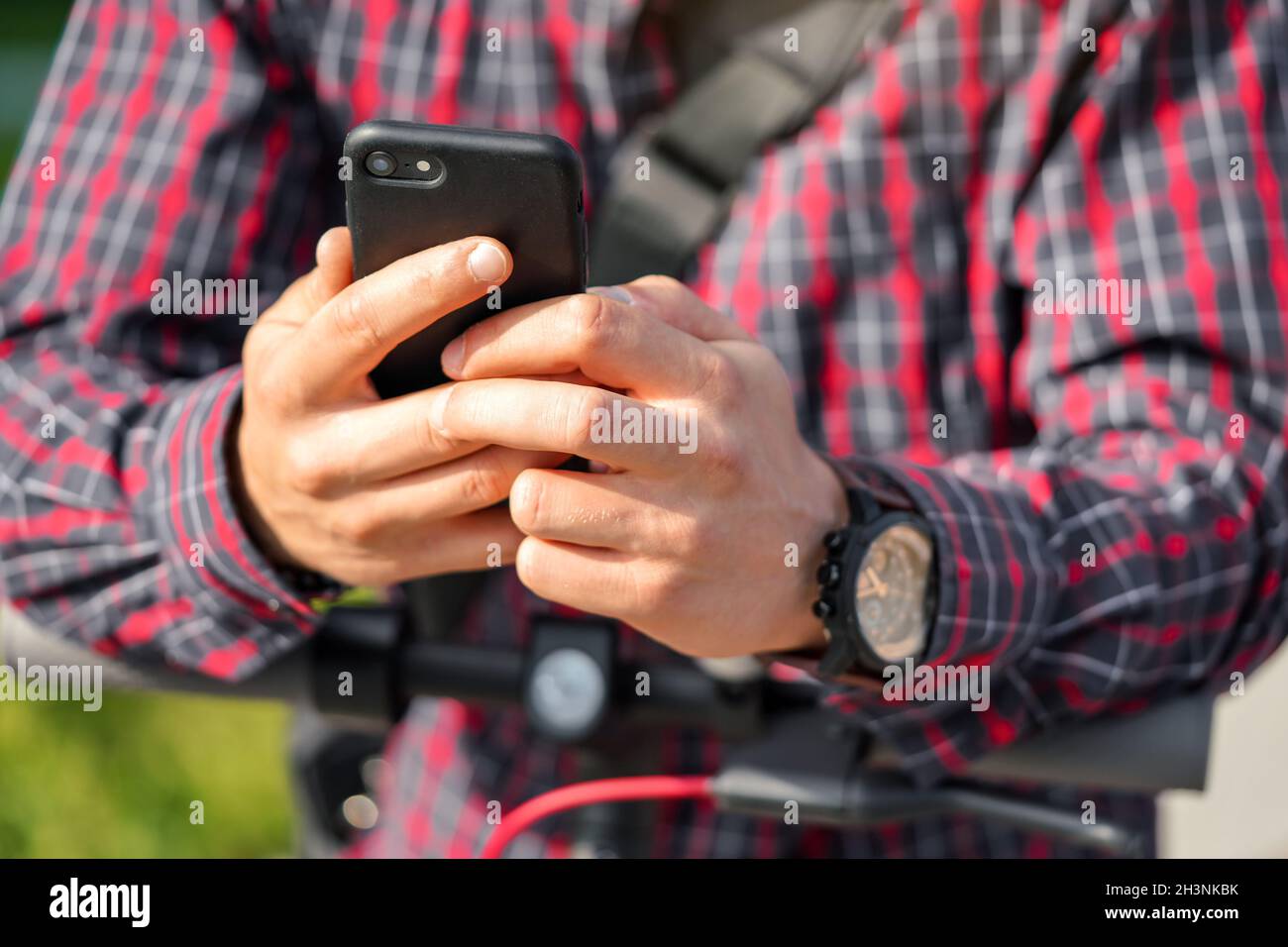 Jeune homme portant une chemise penchée sur un guidon de scooter électrique, tenant le smartphone mobile dans ses mains, détail gros plan Banque D'Images