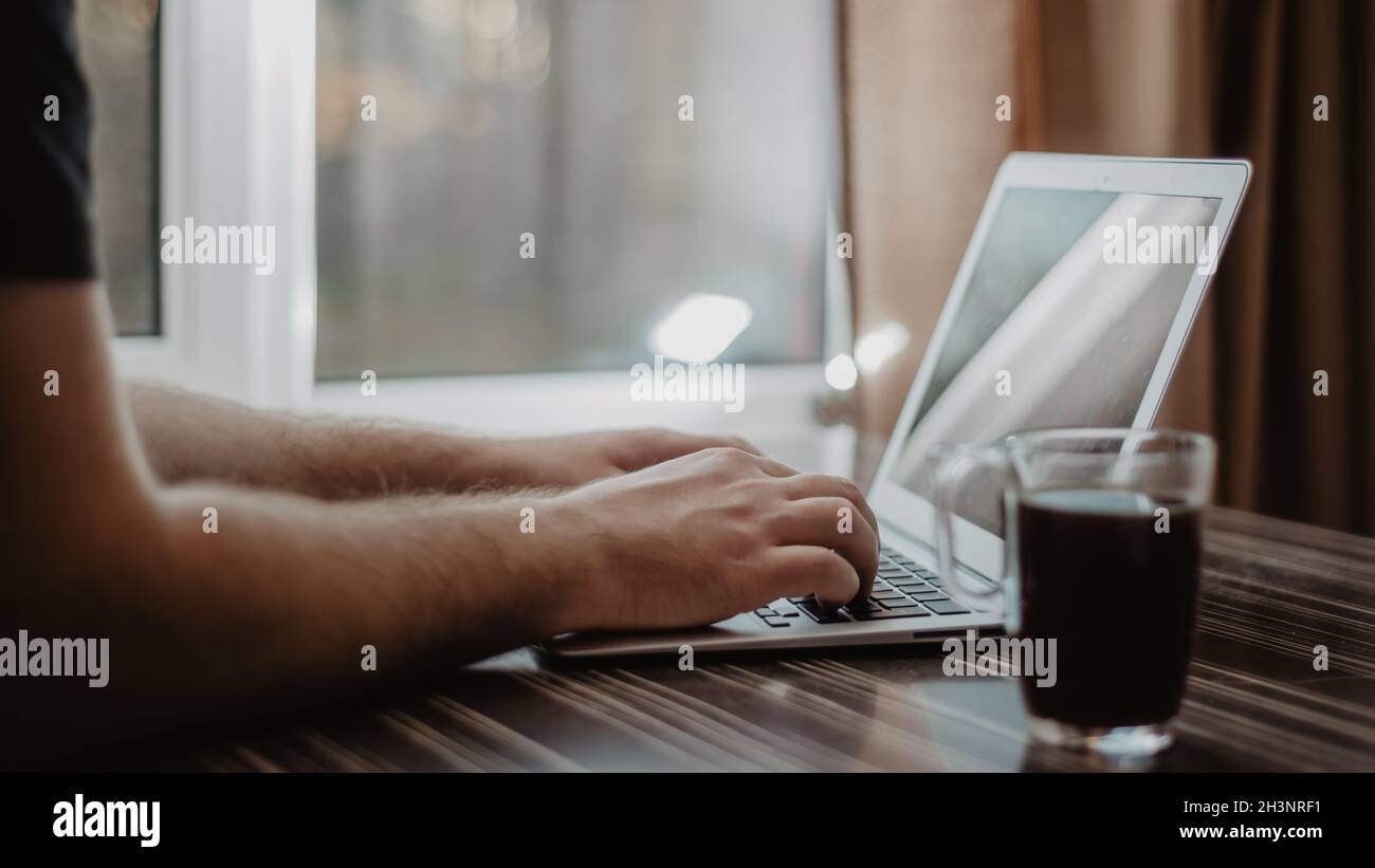 Gros plan d'un homme qui tape sur un ordinateur portable et qui travaille avec un tableau financier sur une table de bureau en bois désordonnée. Banque D'Images