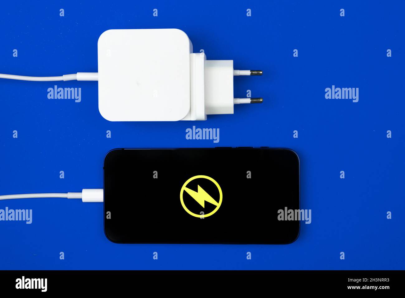 Adaptateur de chargeur pour smartphone.Téléphone portable avec icône d'énergie à l'écran.Arrière-plan bleu, vue de dessus Banque D'Images