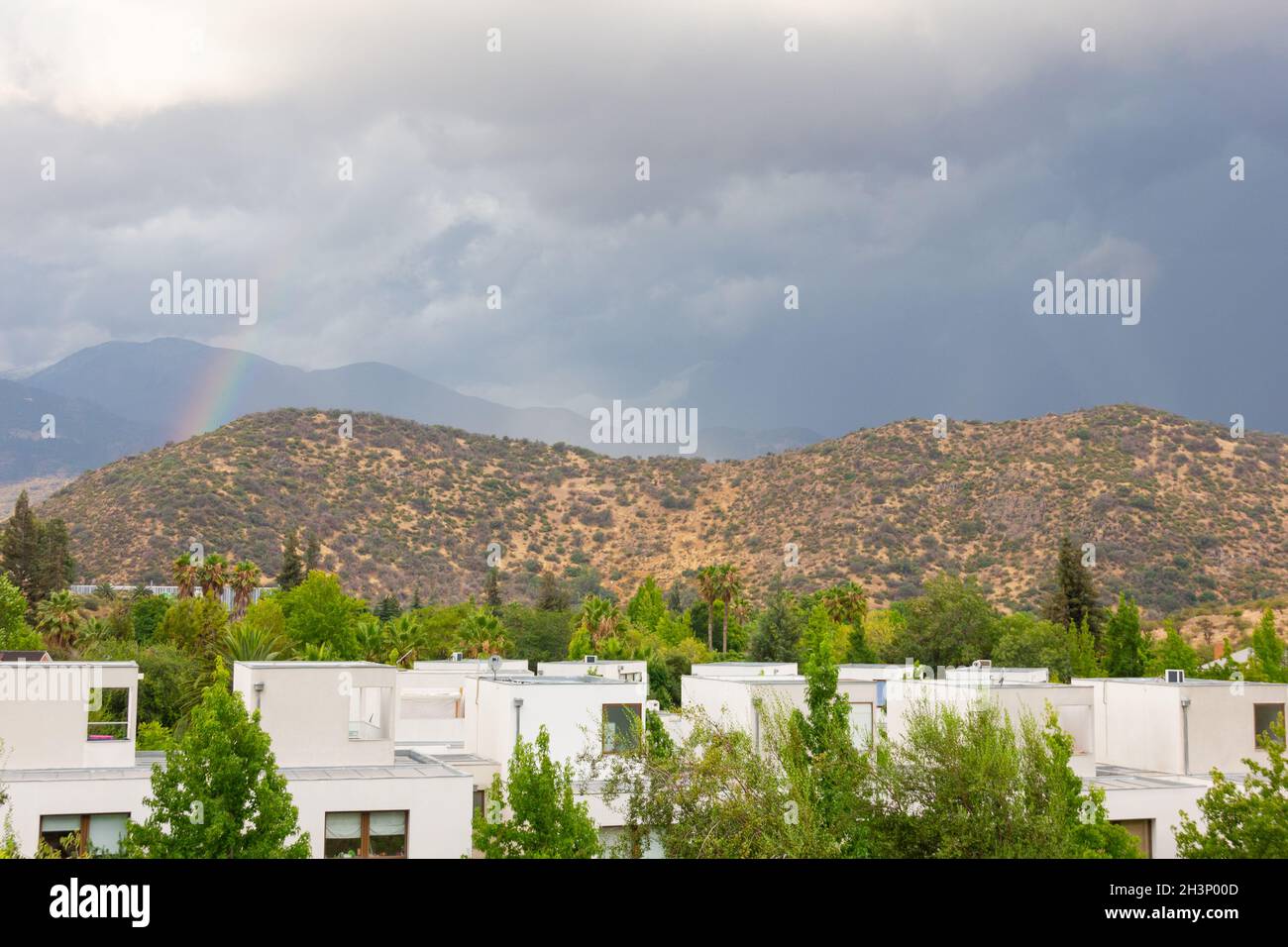 Arc-en-ciel coloré se cachant derrière les montagnes dans la zone résidentielle au ciel nuageux.Concept de paysage naturel menaçant les tempêtes Banque D'Images