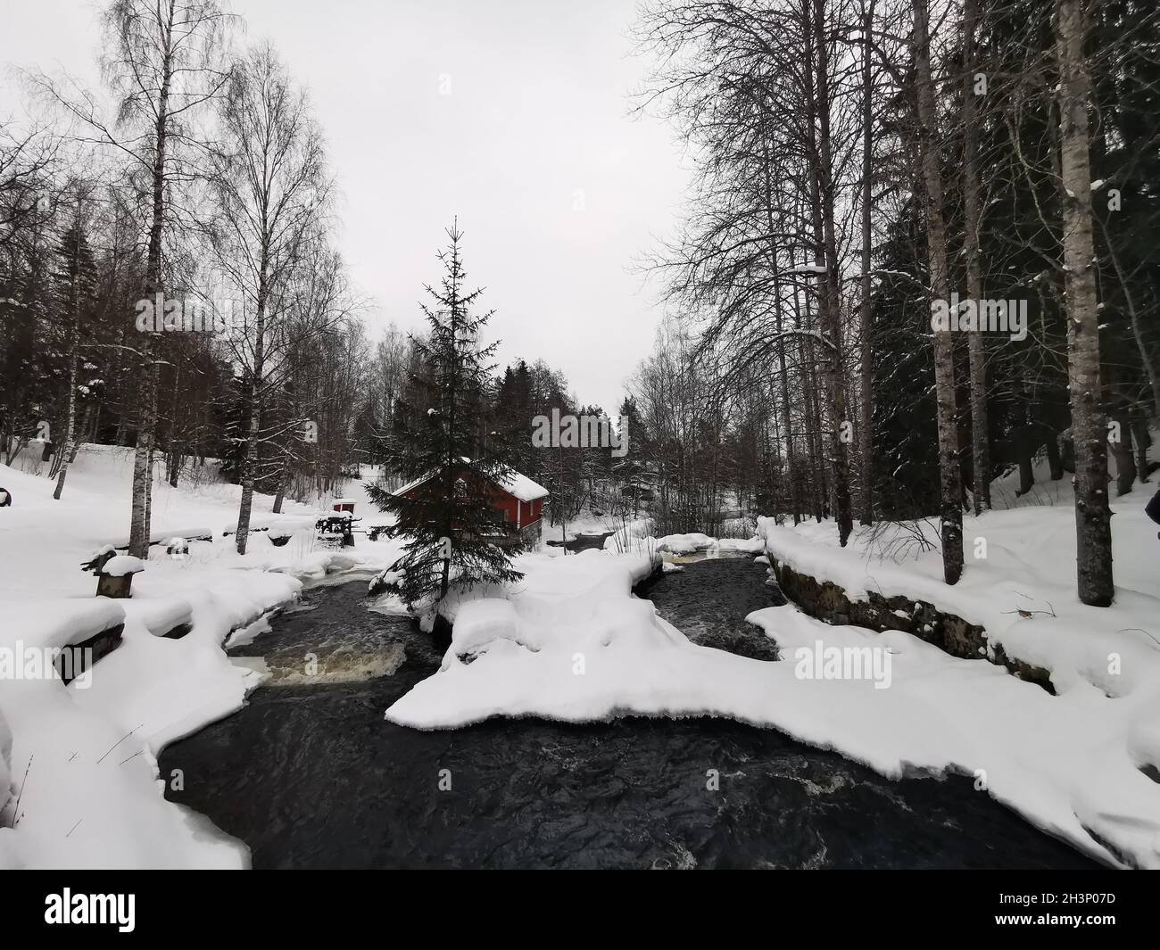 Une jolie cabane en bois rouge construite sur la rivière en hiver.Recouvert de neige. Banque D'Images
