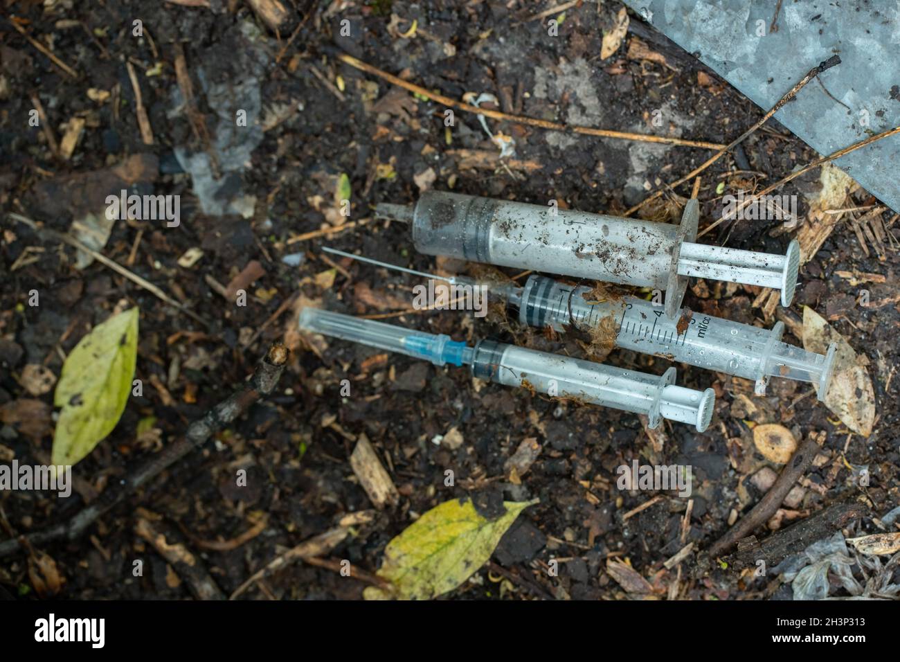 bouquet de seringues sales utilisées calfeutées après l'injection de médicaments couché sur le sol à l'extérieur Banque D'Images