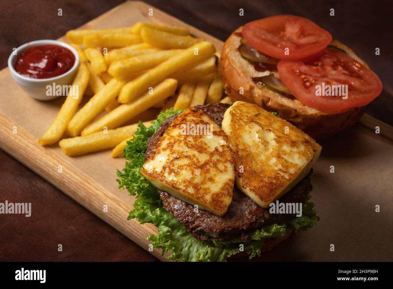 Hamburger de bœuf au fromage grillé semi-fini, servi avec des frites et des tomates sur un trey décoratif en bois avec une sauce tomate.F Banque D'Images