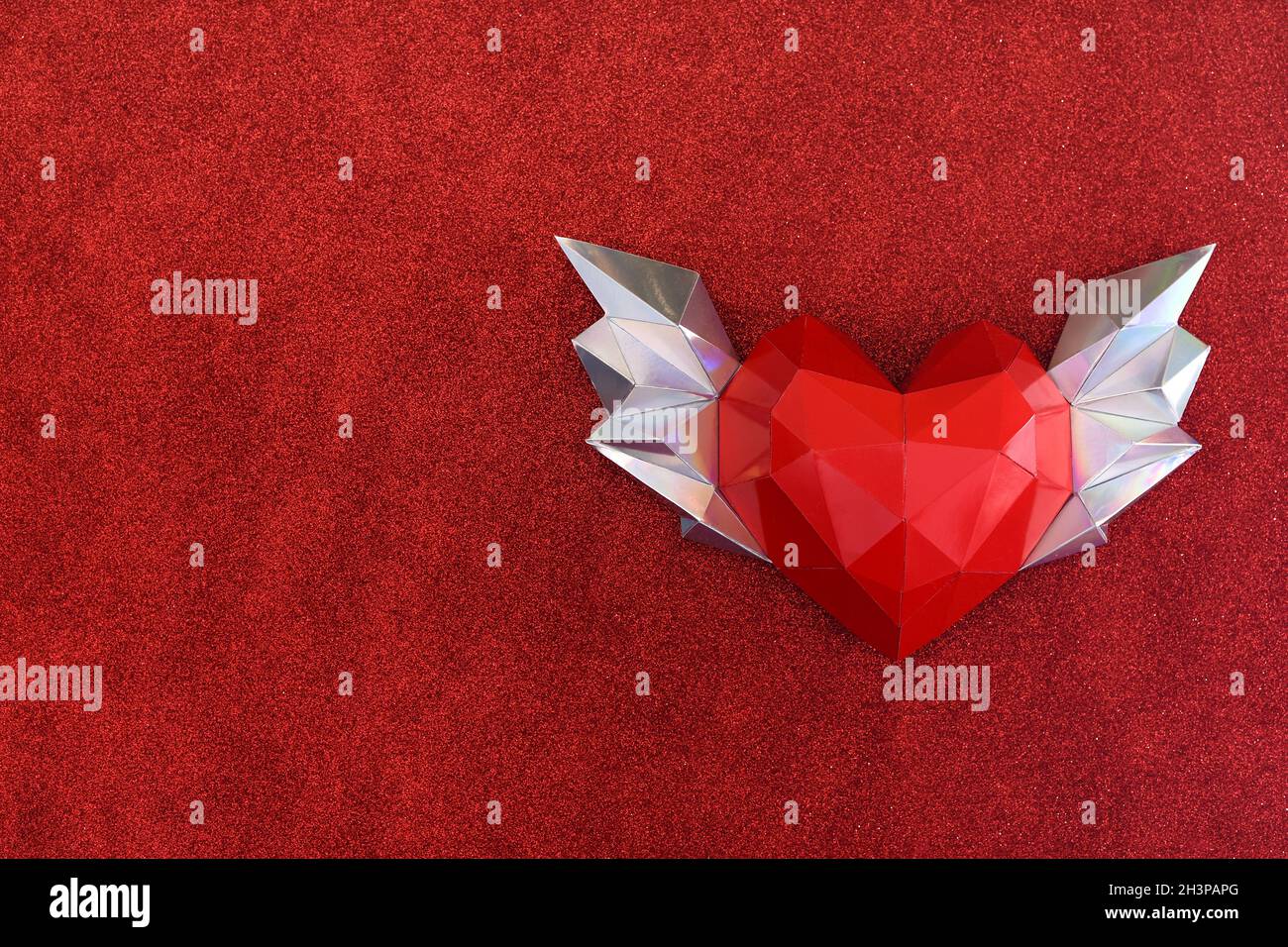 Coeur polygonal avec ailes sur un arrière-plan rouge doux. Espace de copie Banque D'Images