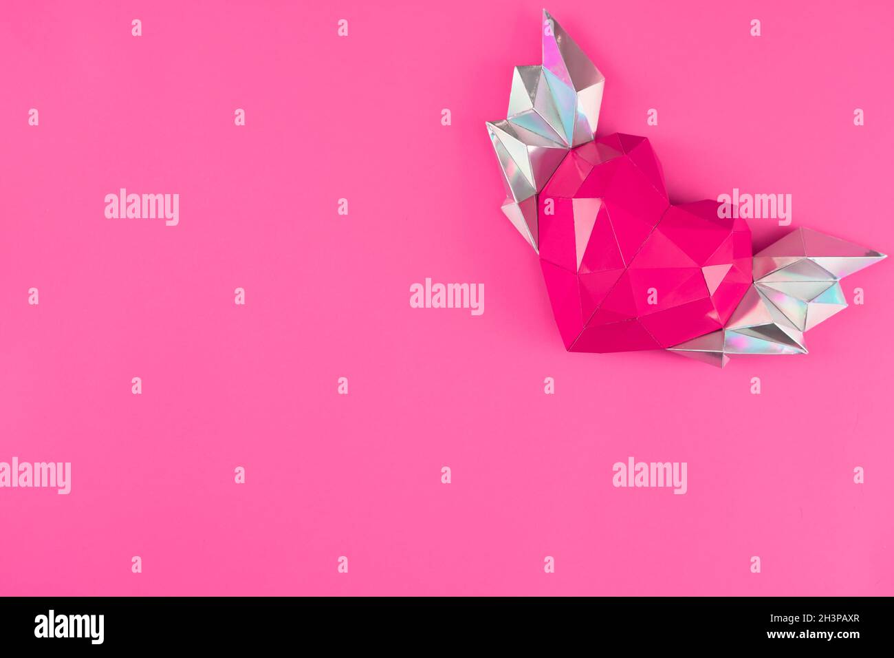 Coeur en papier polygonal avec ailes sur fond rose. Banque D'Images