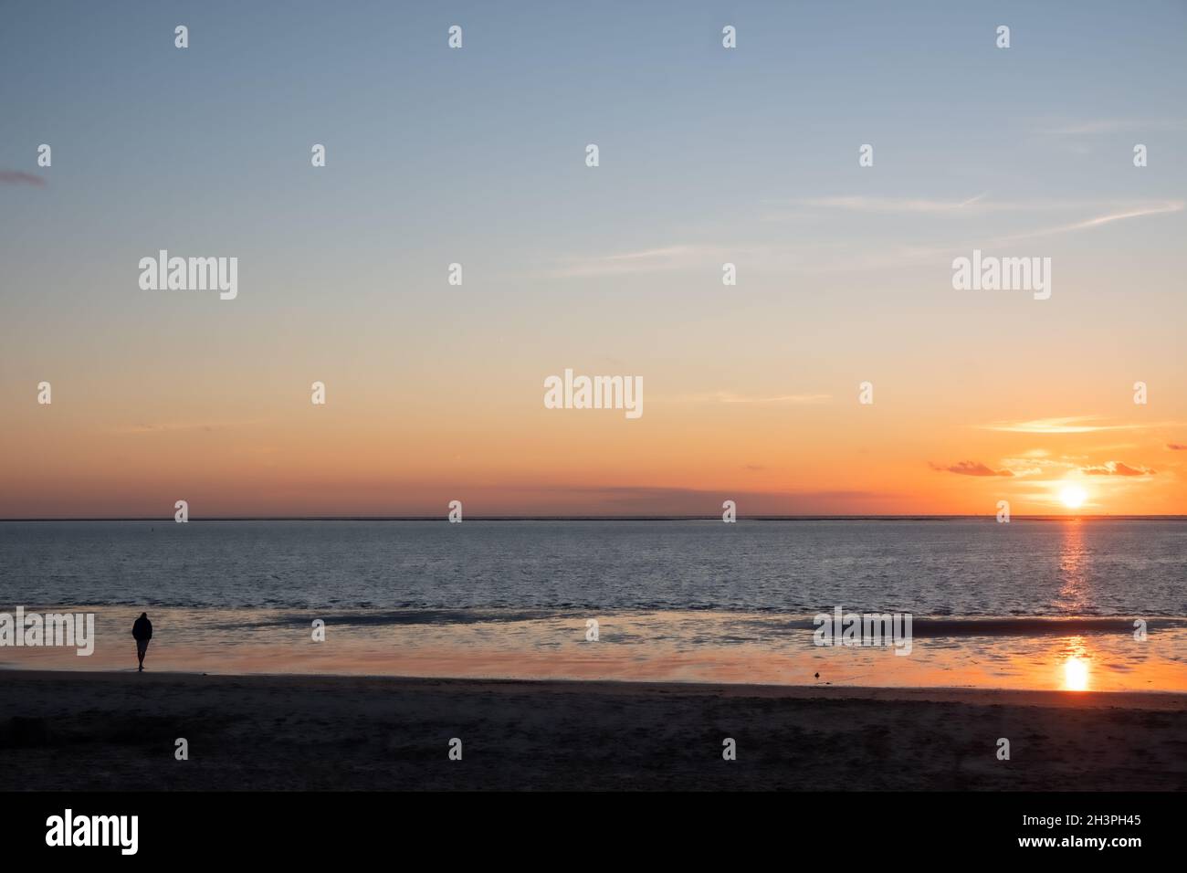 Vue sur les silhouettes des personnes marchant dans le soleil couchant sur la mer et réfléchi sur la plage, nuages avec le soleil brillant Banque D'Images