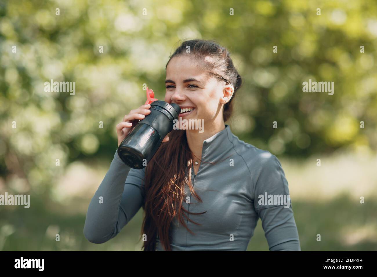 Femme de chemin fatiguée jogger boire de l'eau en bouteille après avoir fait du jogging dans le parc à l'extérieur. Banque D'Images