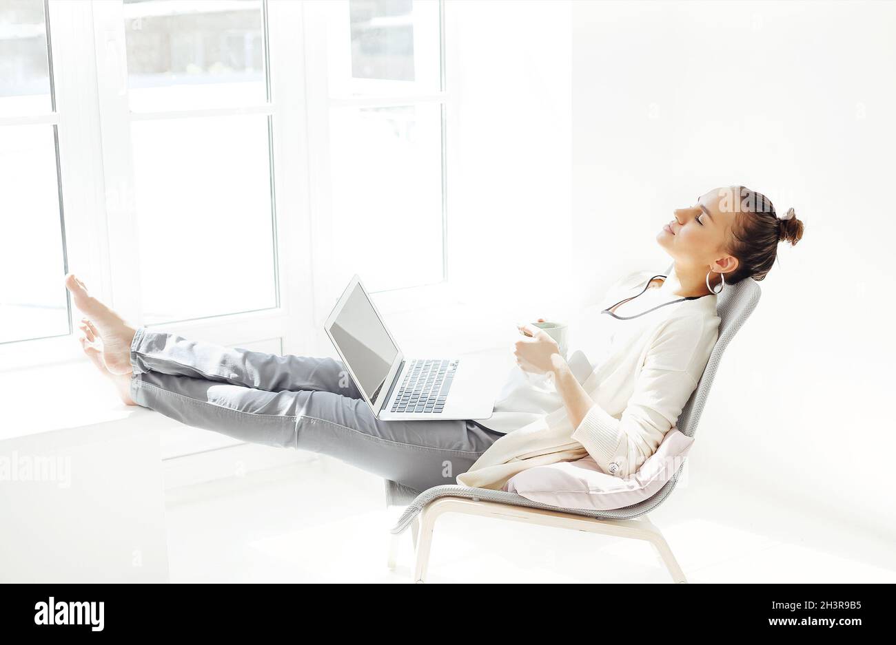 Jeune femme avec les mains derrière la tête assise sur une chaise et se détendant avec les yeux fermés après avoir utilisé un ordinateur portable Banque D'Images