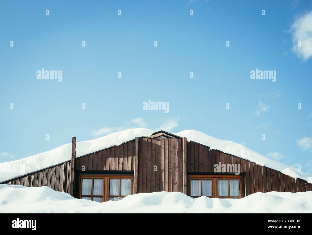 Maison moderne en bois avec fenêtres et neige sur le toit, ciel bleu avec espace texte Banque D'Images