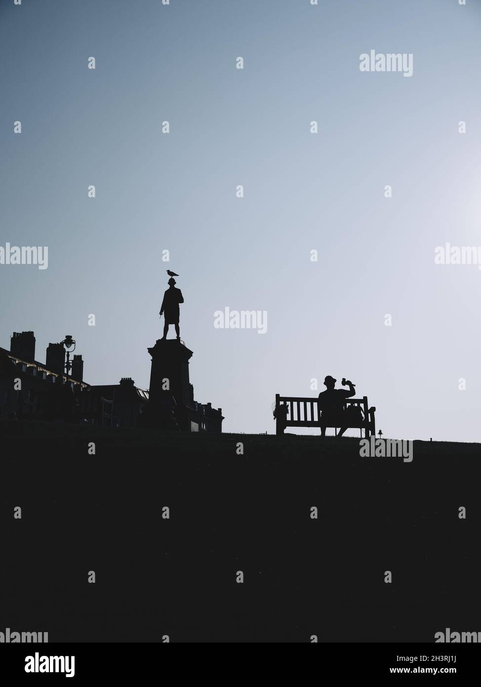 Une silhouette sombre figure ombre d'une statue avec un mouette perché sur la tête et un touriste assis sur un banc public - bord de mer britannique Banque D'Images