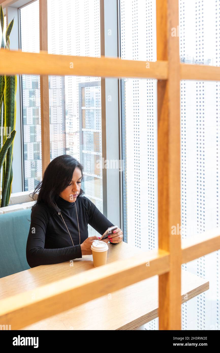 Belle femme pensive brunette tout en ayant un café et réviser votre téléphone cellulaire Banque D'Images