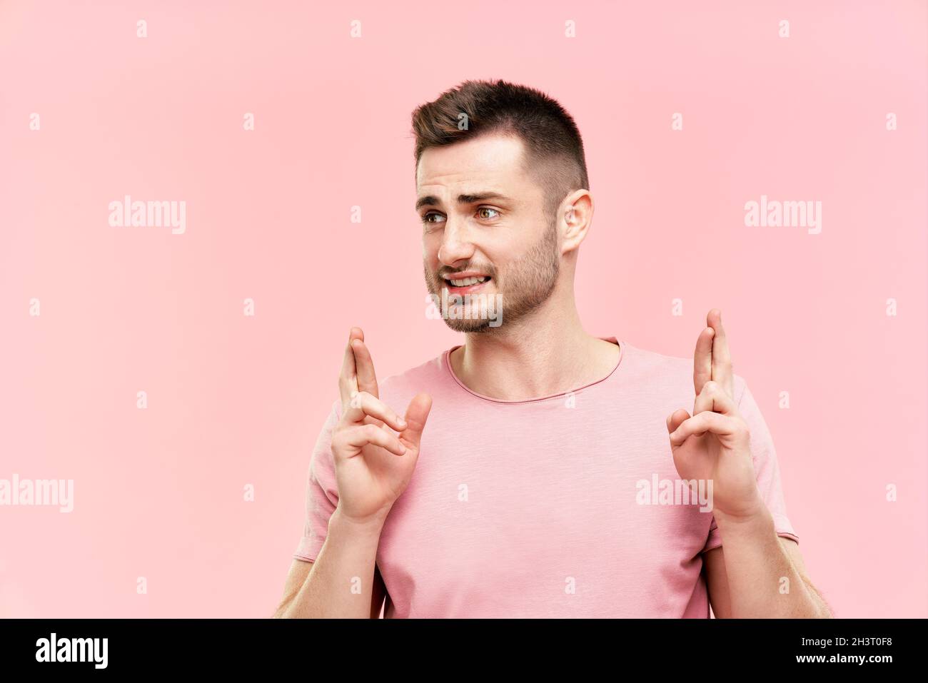 Jeune homme beau croisant ses doigts et souhaitant bonne chance sur fond rose Banque D'Images