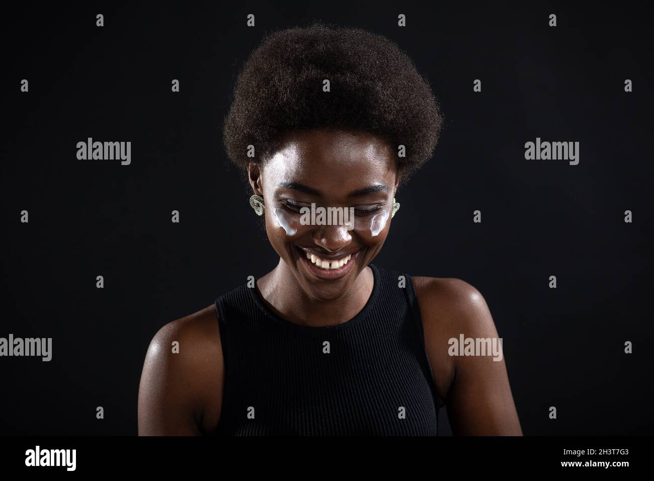 Belle jeune femme noire afro-américaine d'origine ethnique appliquant de la crème blanche hydratante sur son visage Banque D'Images