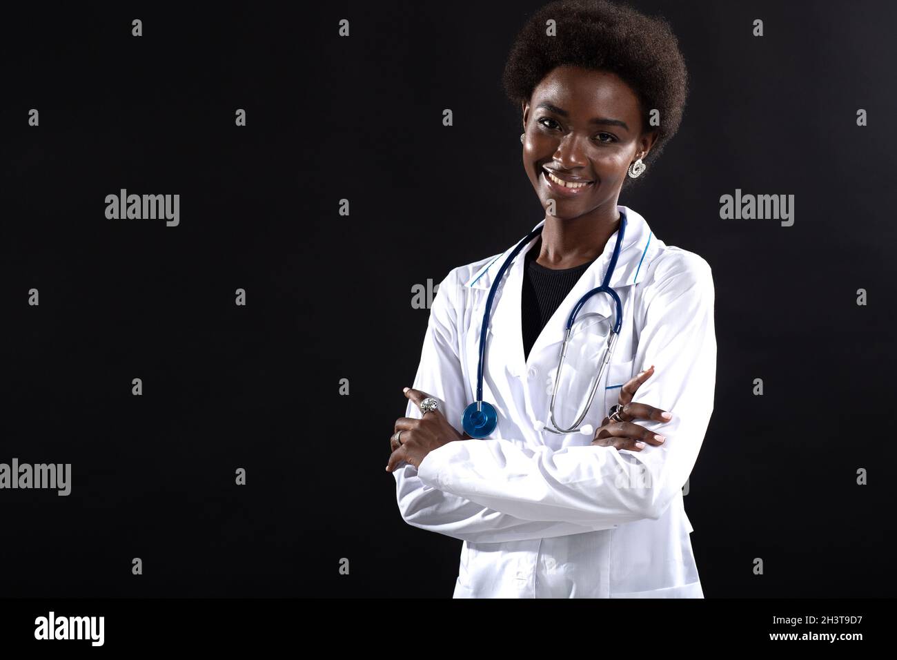 Femme noire médecin souriant sur fond noir.Femme afro-américaine en robe médicale avec stéthoscope debout et souriant Banque D'Images