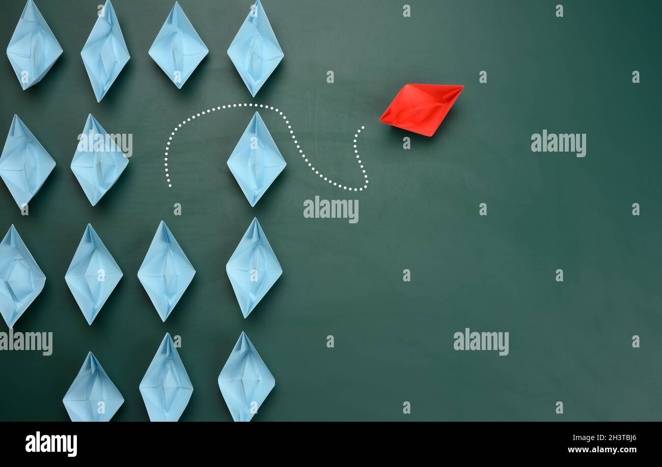 Groupe de bateaux en papier bleu naviguent dans une direction, un rouge navigue dans la direction opposée Banque D'Images