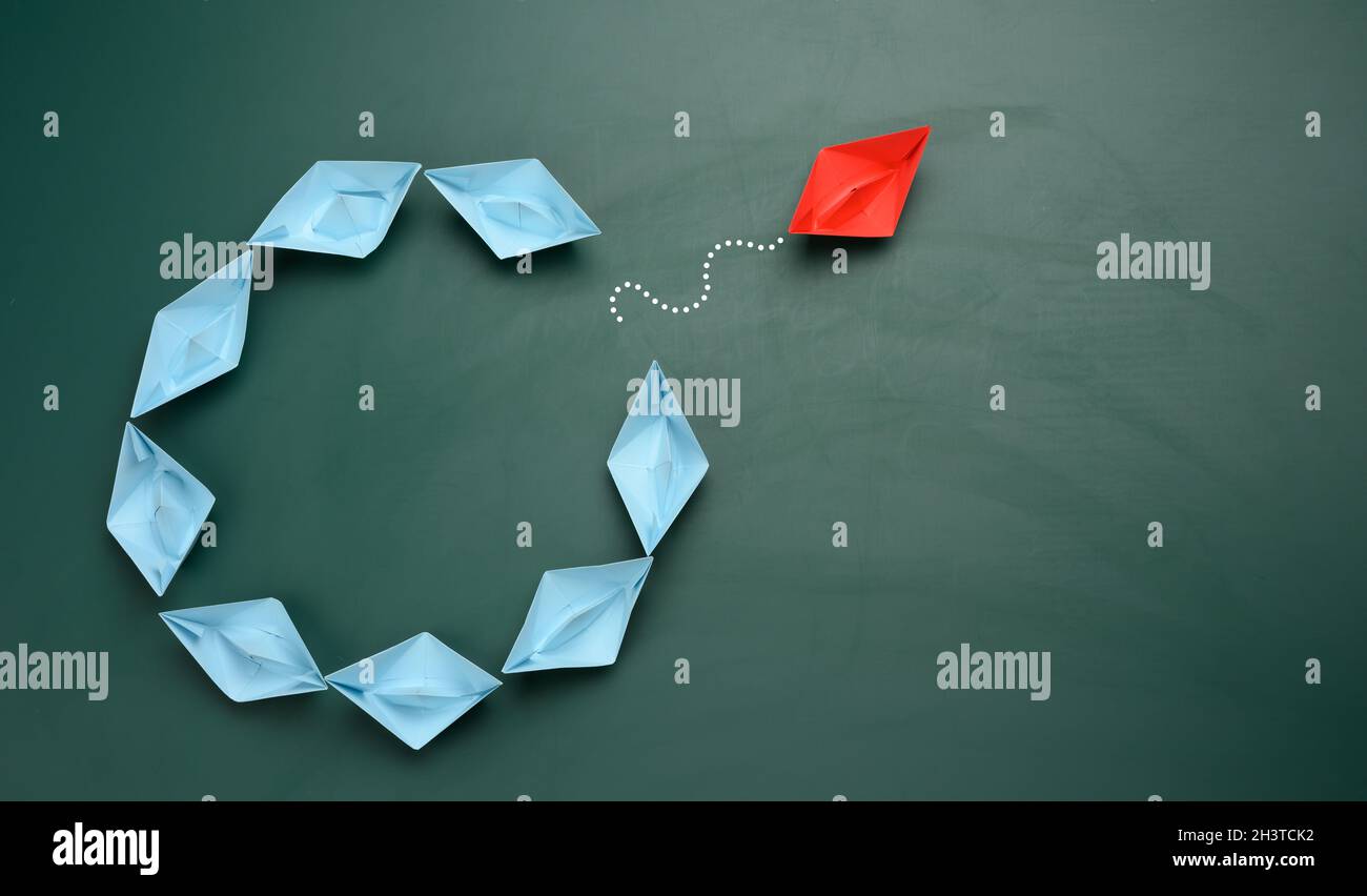 Groupe de bateaux en papier bleu naviguent dans une direction, un rouge navigue dans la direction opposée Banque D'Images