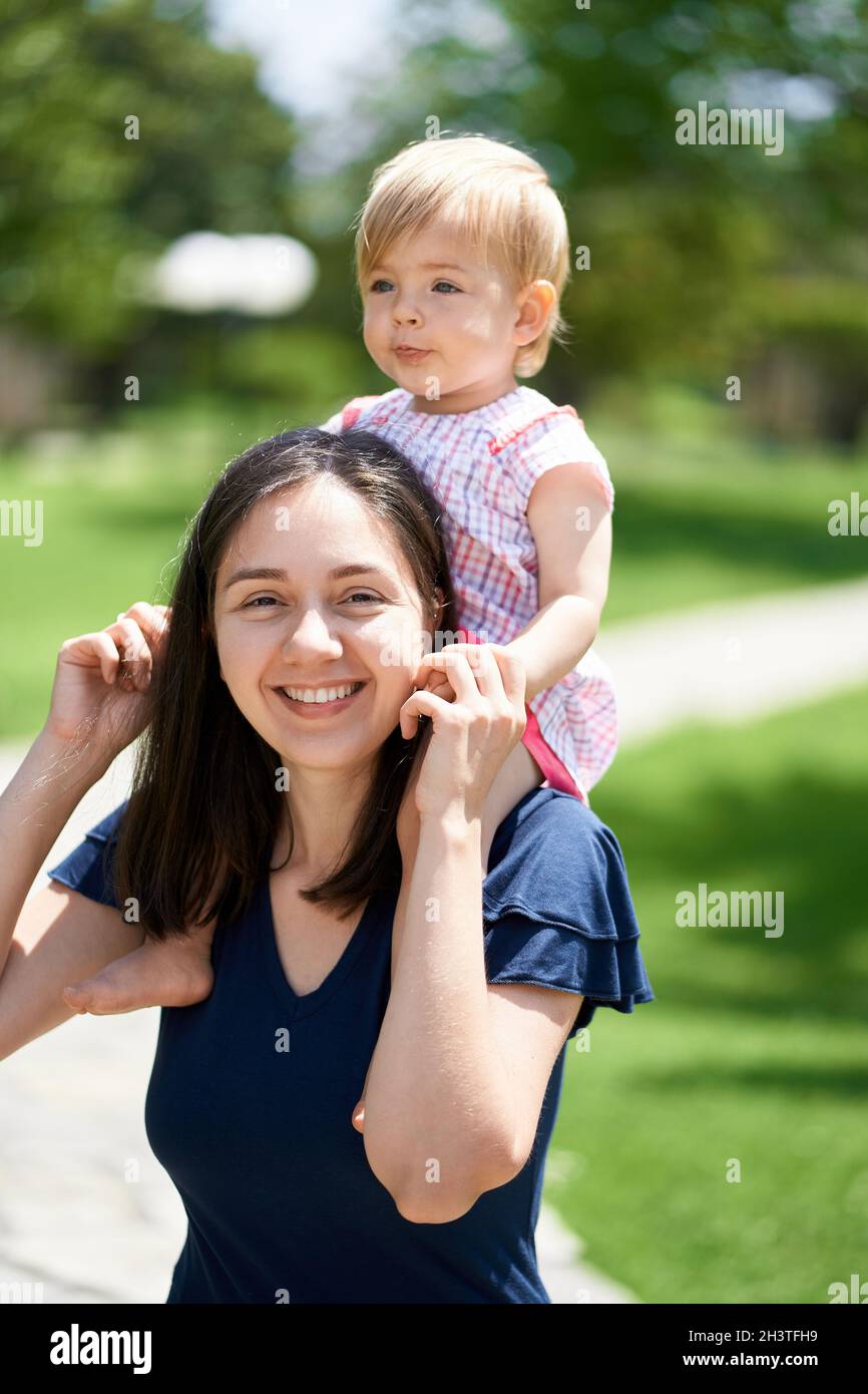 Une maman souriante porte une petite fille sur ses épaules, la tenant avec ses mains Banque D'Images