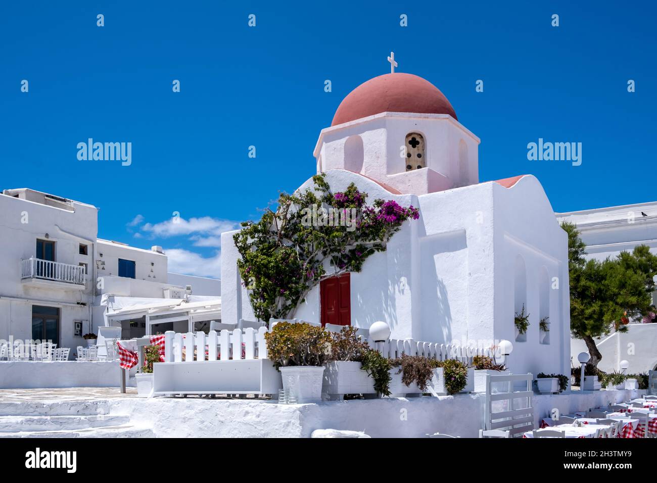 Chapelle blanche sur ciel bleu clair.Église à dôme rouge dans la ville de Chora, île de Mykonos, Cyclades.Grèce.Tables et chaises de taverne en plein air, jour ensoleillé Banque D'Images