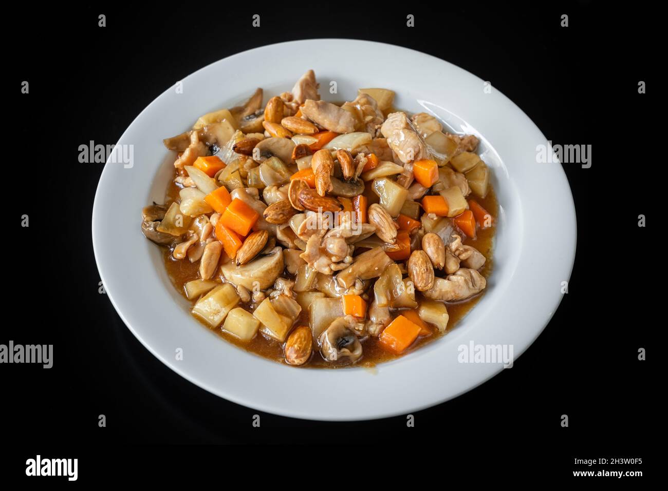 Un plat chinois traditionnel de ragoût de poulet, avec des amandes, des carottes et des pâtes.Dans une plaque sur fond noir, gros plan. Banque D'Images