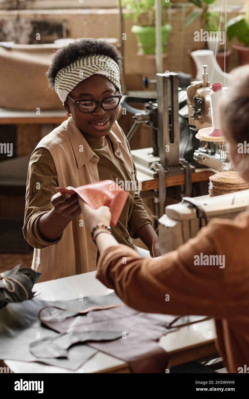 Une jeune femme africaine discutant de la pièce de cuir avec sa collègue pendant qu'elle coudre sur des machines à coudre dans l'atelier Banque D'Images