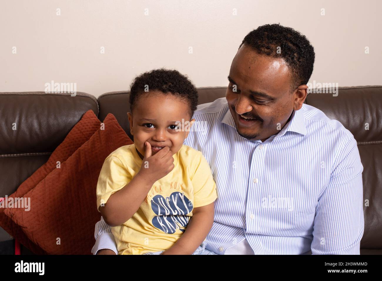 Portrait riant d'un jeune garçon de 2 ans avec son père, assis sur un canapé à la maison Banque D'Images