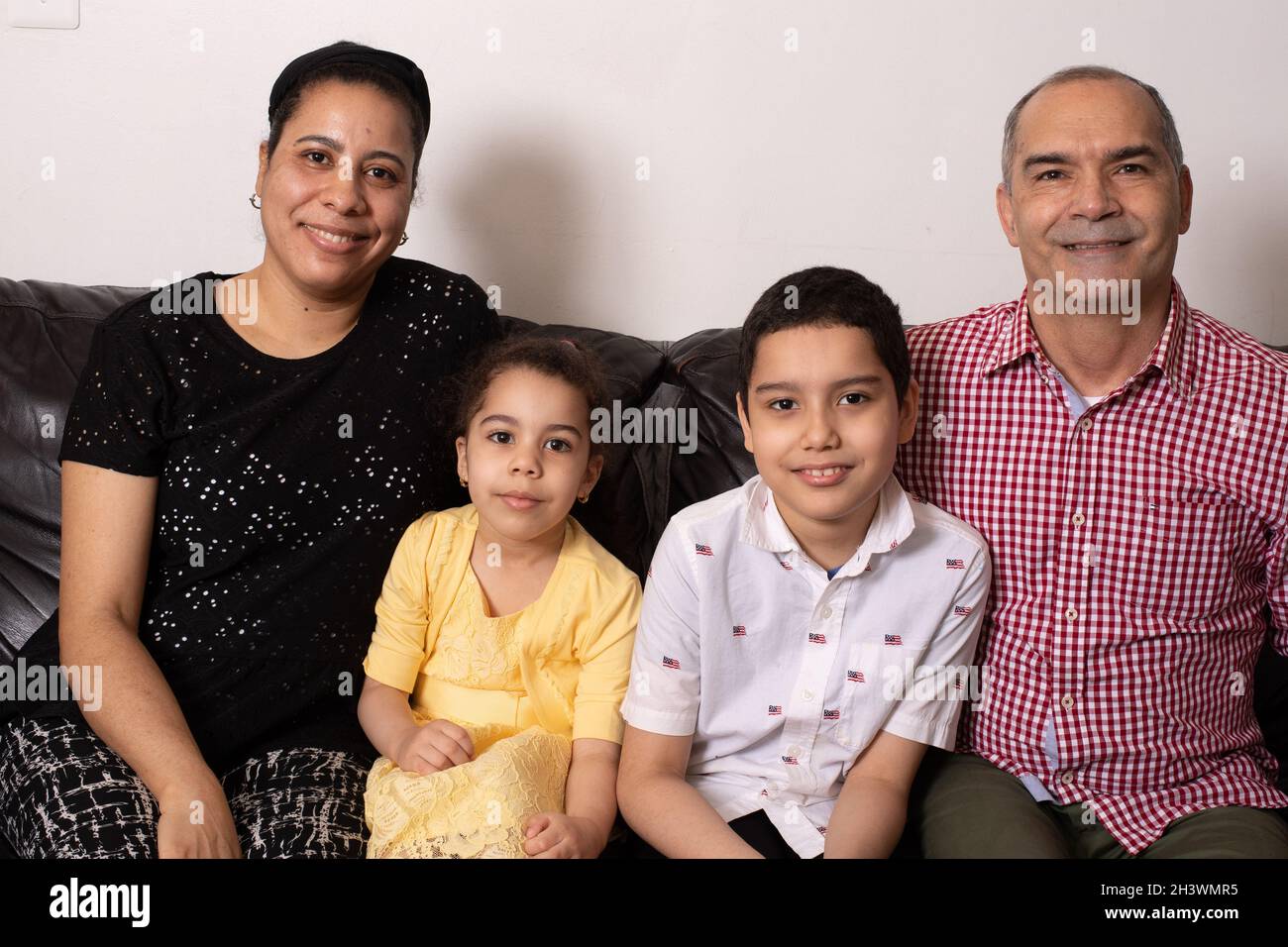 Portrait de famille assis ensemble sur un canapé, fille de 4 ans, frère de 9 ans, mère et père, tous regardant la caméra Banque D'Images