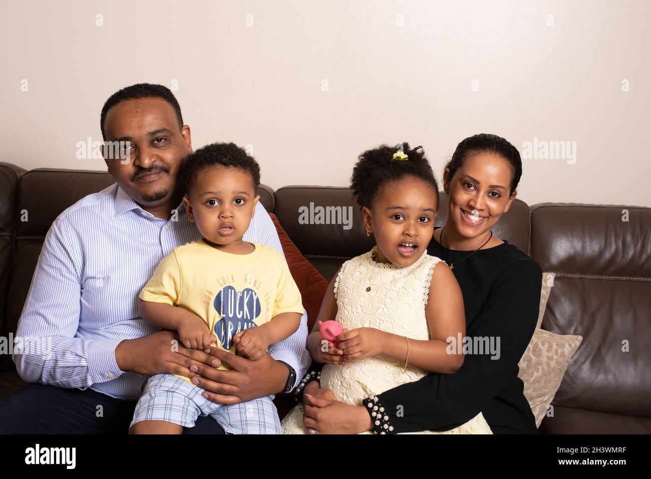 Famille à la maison, assis sur un canapé, fille de 5 ans, frère de 2 ans, mère et père, tous regardant la caméra Banque D'Images