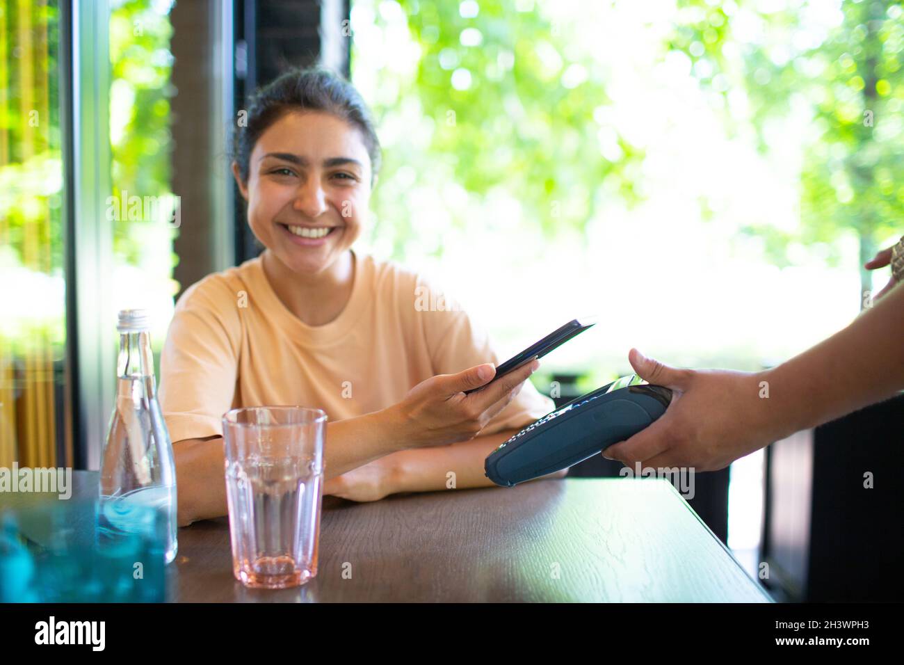 La femme indienne paie avec le téléphone mobile nfc sans contact terminal de paiement dans le café-bar. Banque D'Images