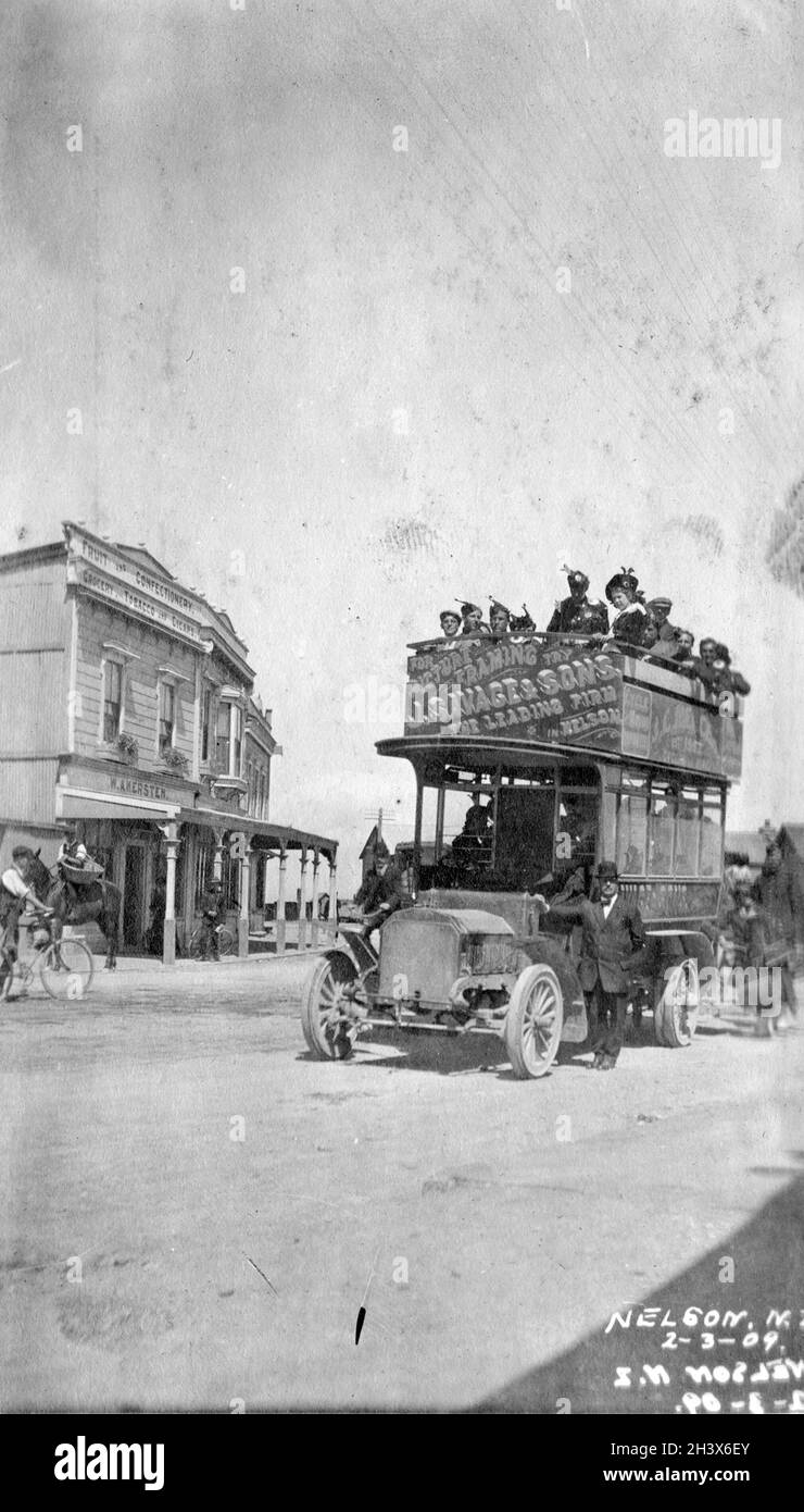 Des membres de la Kilties, une bande canadienne de Scots, à bord d'un autobus à toit ouvert à Nelson, en Nouvelle-Zélande, devant l'épicerie de W. Akersten, 1909.La signalisation au niveau supérieur, qui tient plusieurs membres du Kilties Band, annonce J. Savage et fils, cadrage d'image. Banque D'Images