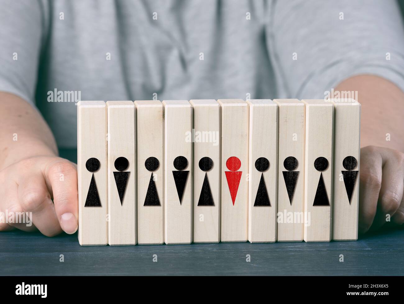 Deux mains femelles tiennent des cubes en bois avec des petits hommes sur une table bleue.Concept de soin d'équipe, choix du leader, cohésion d'équipe Banque D'Images