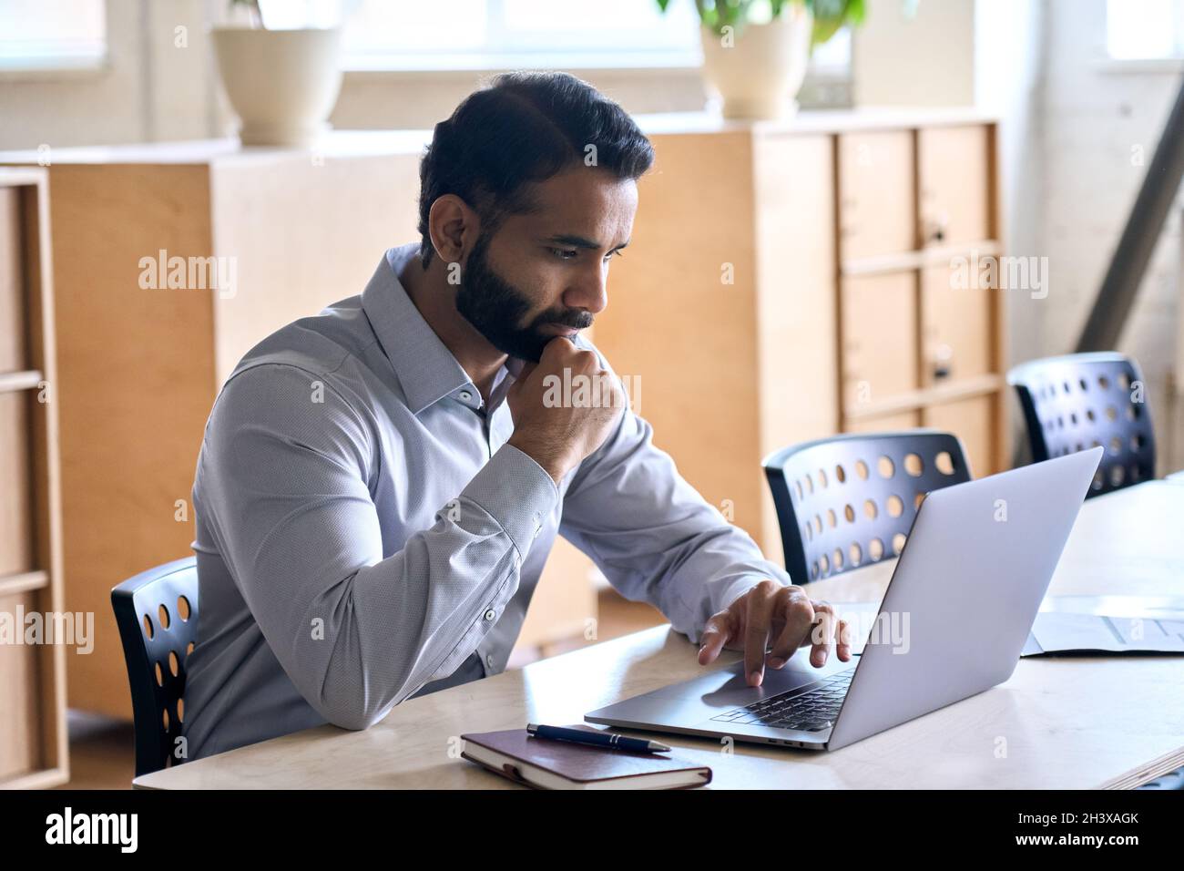 Homme d'affaires indien concentré travaillant dans un bureau moderne avec un ordinateur portable. Banque D'Images