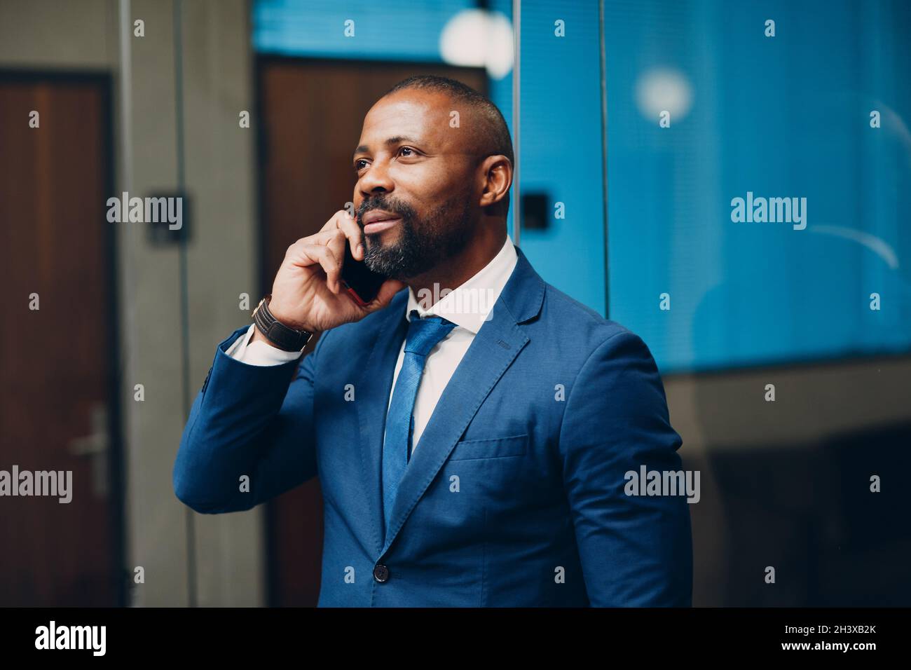 Portrait souriant homme d'affaires afro-américain en costume bleu au bureau avec téléphone mobile parlant sourire. Banque D'Images