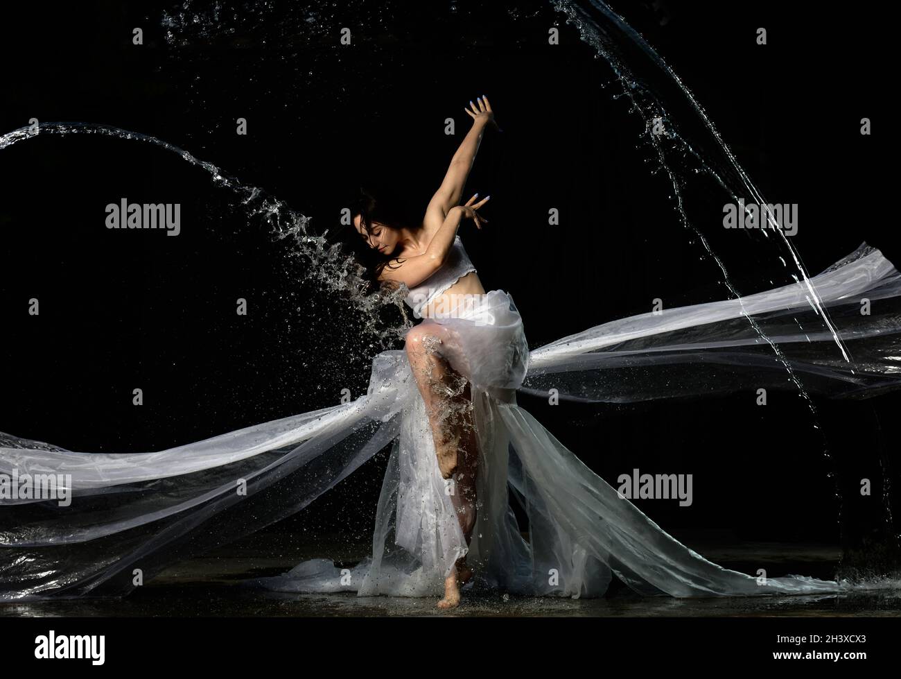 Jeune belle femme d'apparence caucasienne avec de longs cheveux danse dans des gouttes d'eau sur un fond noir Banque D'Images