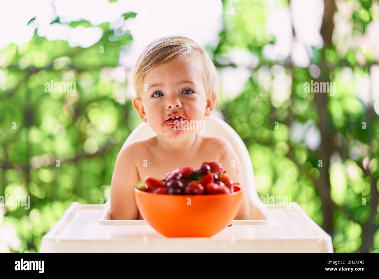 Un enfant au visage sale est assis à une table devant une assiette de fruits Banque D'Images