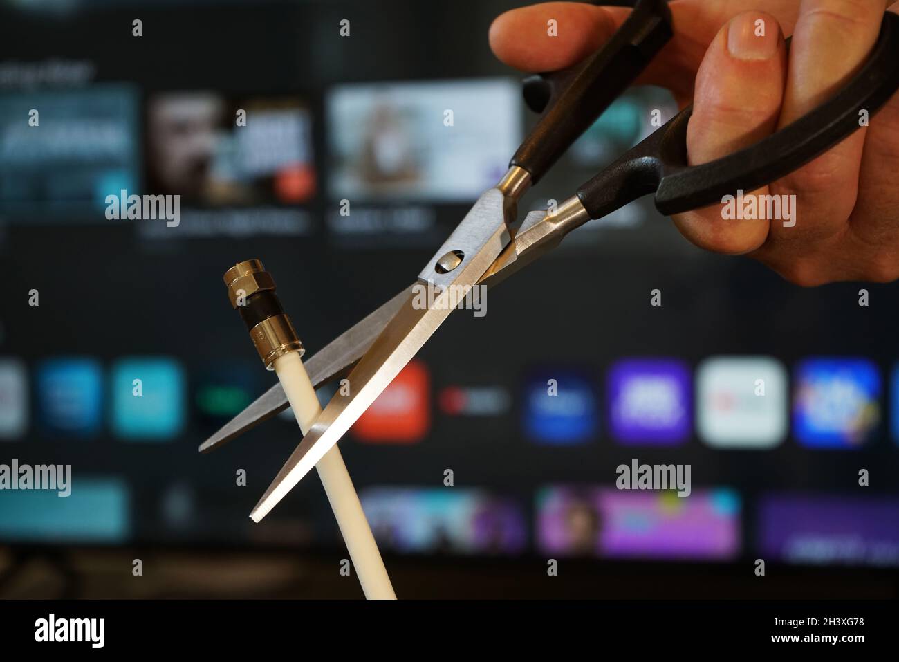 Ciseaux coupant à travers un câble coaxial avec TV hors foyer en arrière-plan - couper le concept de TV par câble Banque D'Images