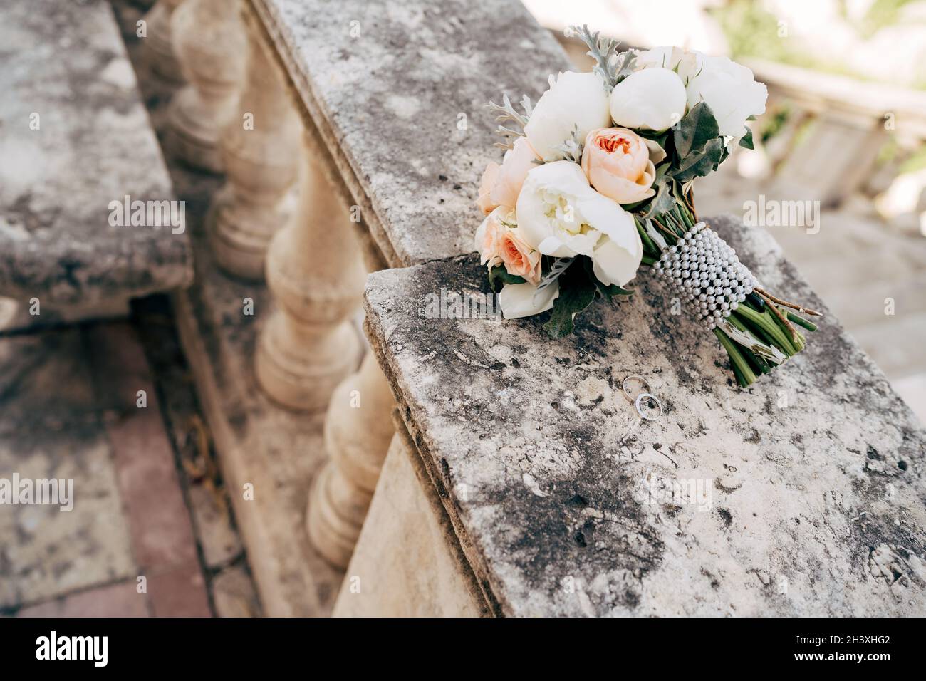 Bouquet de mariée de péonies blanches et crème, roses, salal, artemisia avec ruban de perle sur la balustrade d'un ancien escalier Banque D'Images