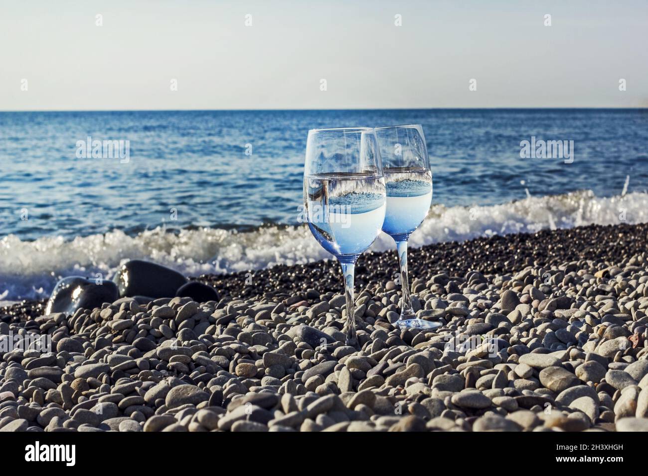 Deux verres d'eau de mer près de la rive sur des galets ensoleillé le matin Banque D'Images