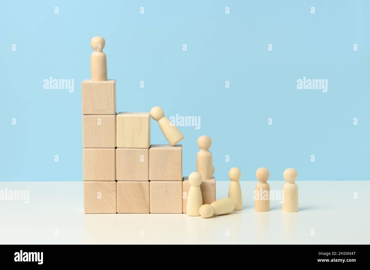 Escaliers de cubes en bois et une foule de figures d'hommes en bois tombés sur un fond bleu. Banque D'Images