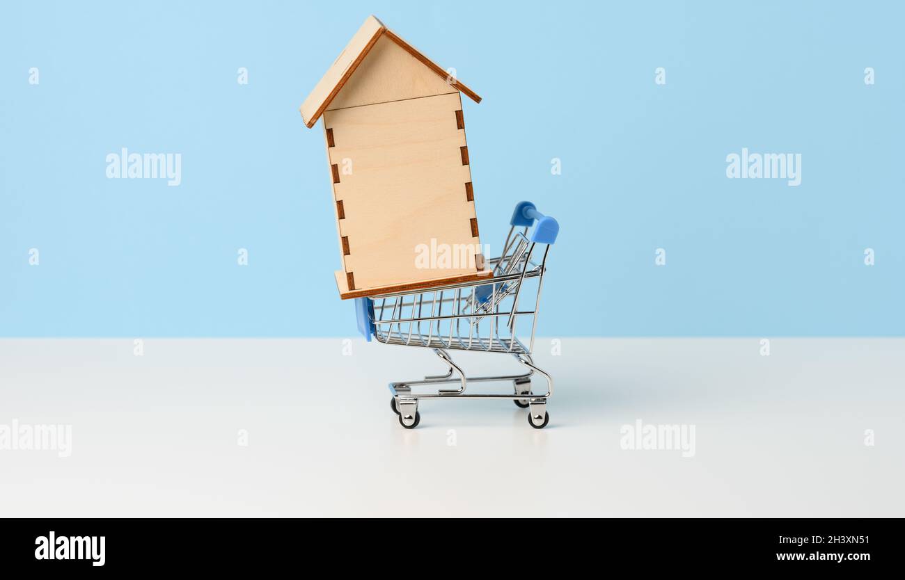 Maison en bois dans un chariot miniature en métal sur fond bleu.Concept d'achat immobilier, hypothèque Banque D'Images