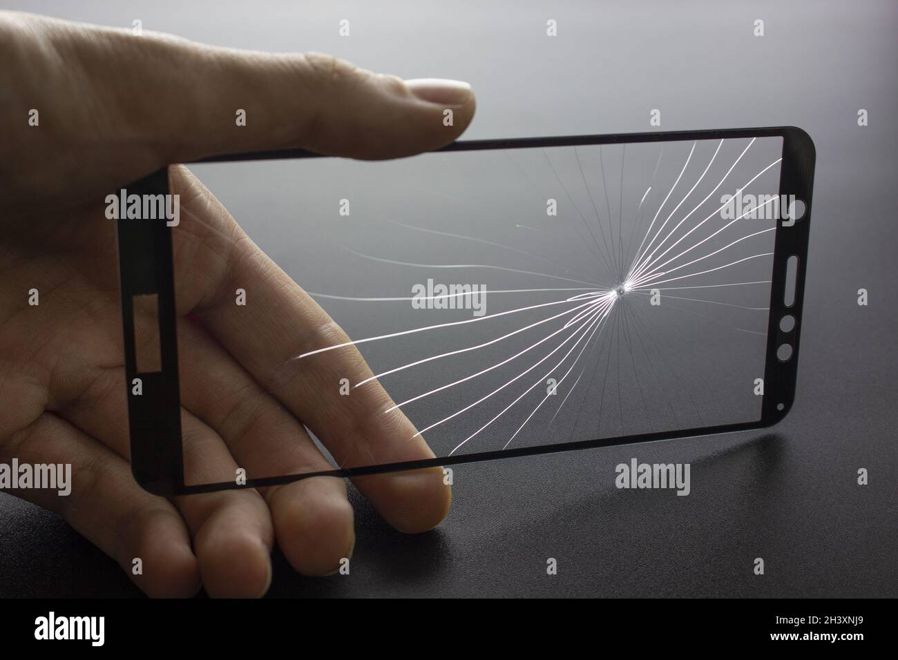 Verre de protection cassé du smartphone avec des fissures à la main sur fond noir. Banque D'Images