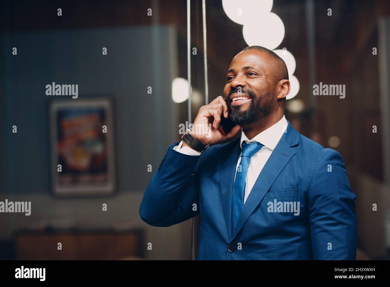 Portrait souriant homme d'affaires afro-américain en costume bleu au bureau avec téléphone mobile parlant sourire. Banque D'Images