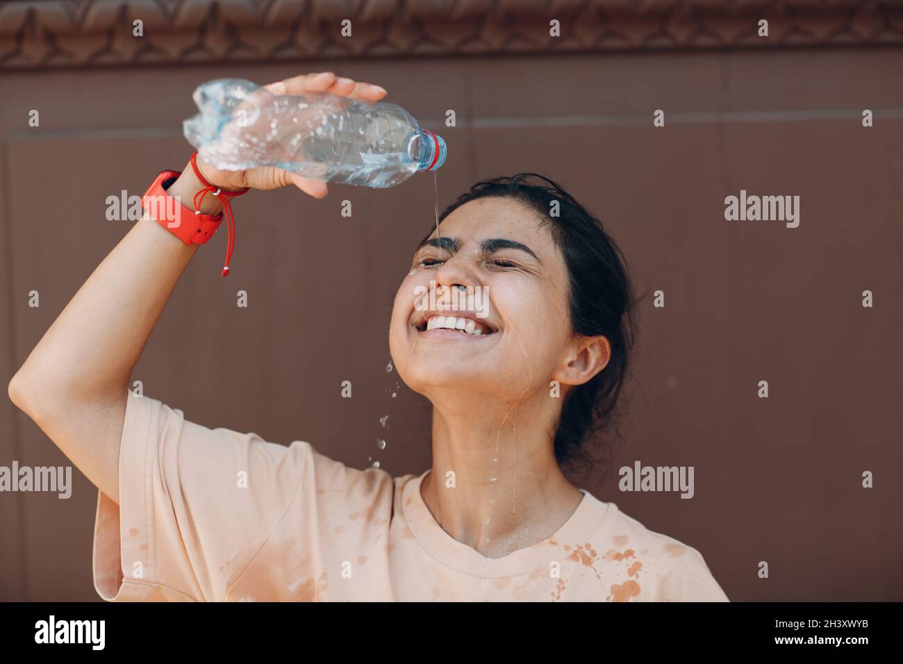 Femme stressée souffrant d'un coup de chaleur rafraîchissant avec de l'eau froide à l'extérieur.Concept de chaleur anormale par temps. Banque D'Images