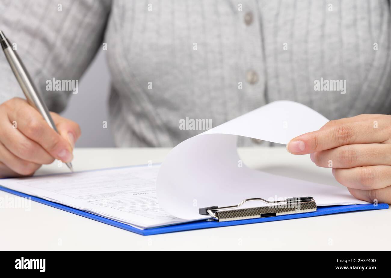 Femme d'apparence caucasienne assis dans des vêtements gris à une table blanche et signe des documents avec un stylo en métal.Homme d'affaires au travail, s Banque D'Images