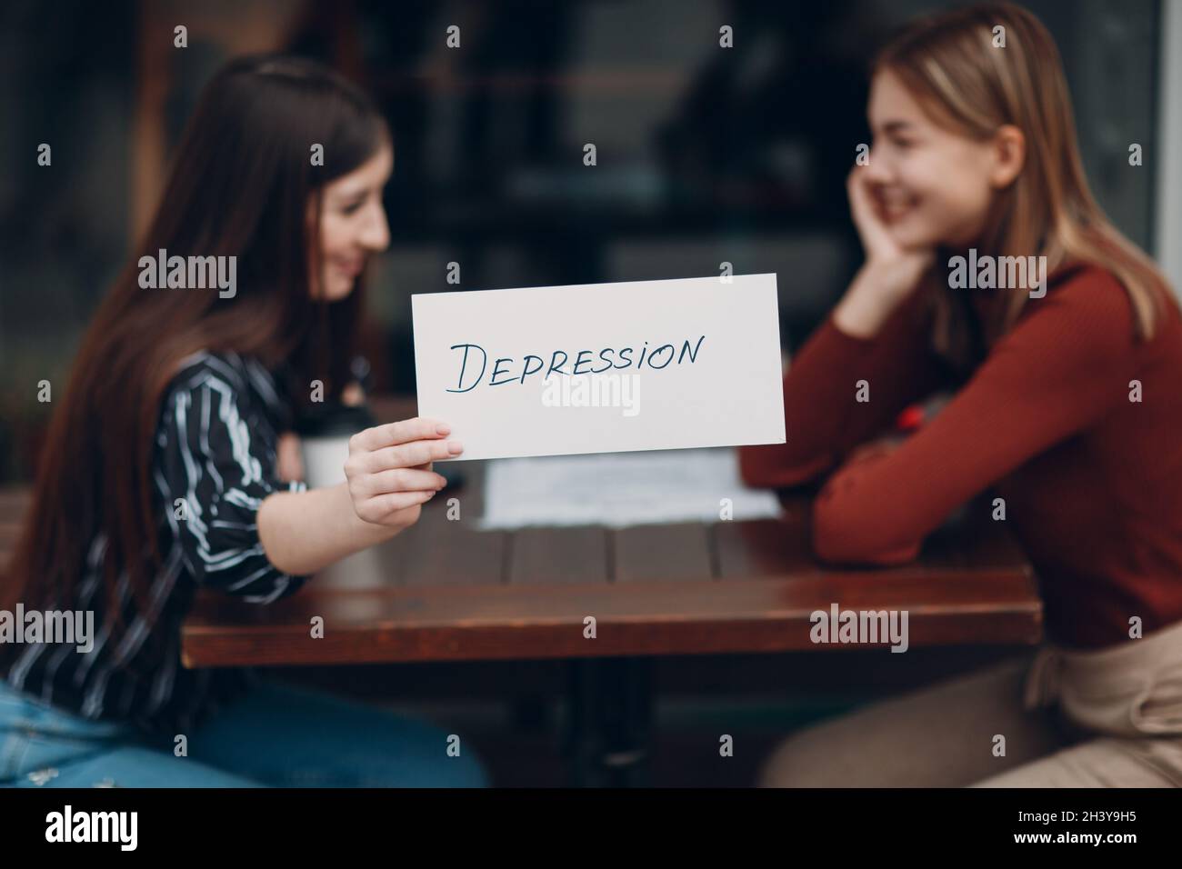 Concept de dépression cachée.Femme tenant une feuille de papier blanc étiquetée dépression mot dans la main.Deux femmes parlant et souriant dans str Banque D'Images