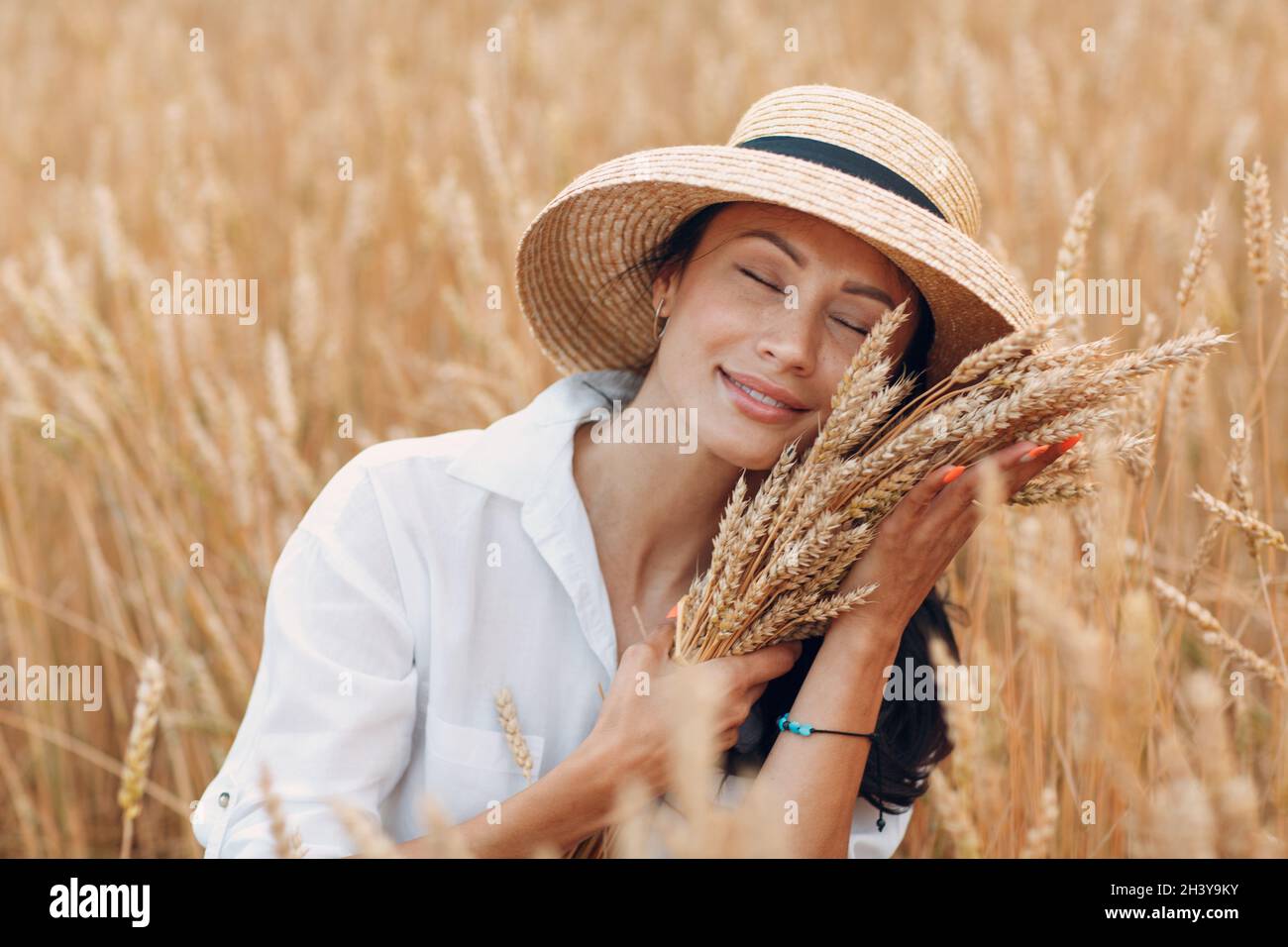 Jeune femme en chapeau de paille tenant une feuille d'épis de blé au champ agricole Banque D'Images