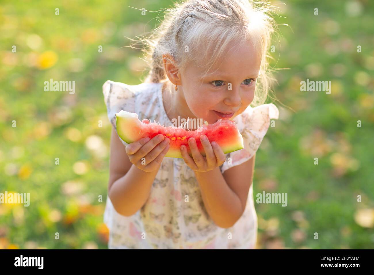 Jolie petite fille blonde mangeant de la pastèque sur l'herbe dans le parc Banque D'Images