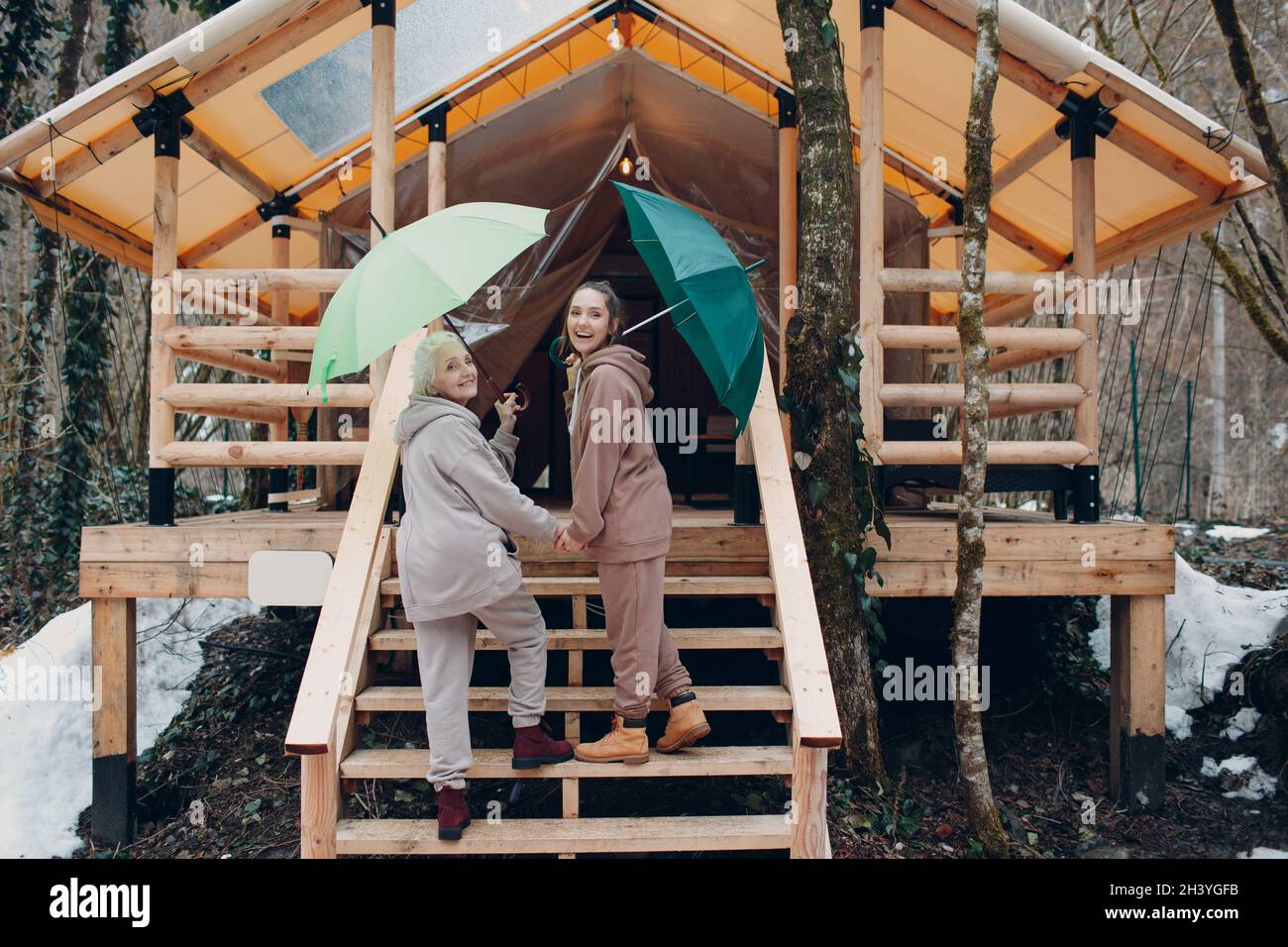 Femmes âgées et jeunes adultes avec parapluie à la tente de camping de glamping.Concept moderne de mode de vie de vacances. Banque D'Images