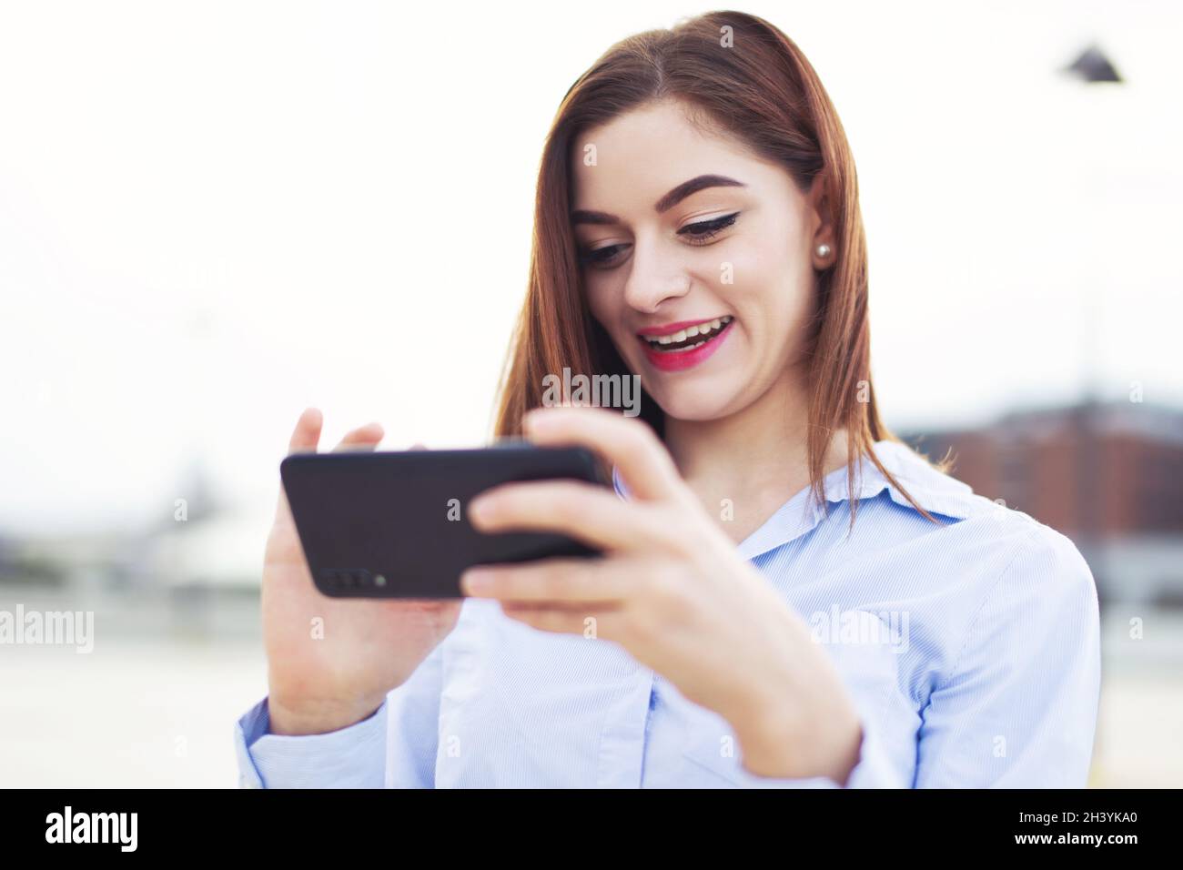 Jeune femme d'affaires caucasienne messagerie par smartphone et rire à l'extérieur Banque D'Images